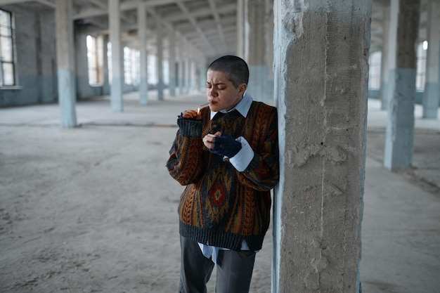 Jeune femme punk sans-abri fumant à peine une cigarette debout sur ses pieds appuyée sur une colonne de béton de soutien se sentant épuisée, affamée et froide