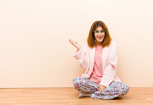 Jeune femme en pyjama assis à la maison, heureuse, surprise et gaie, souriante avec une attitude positive, réalisant une solution ou une idée