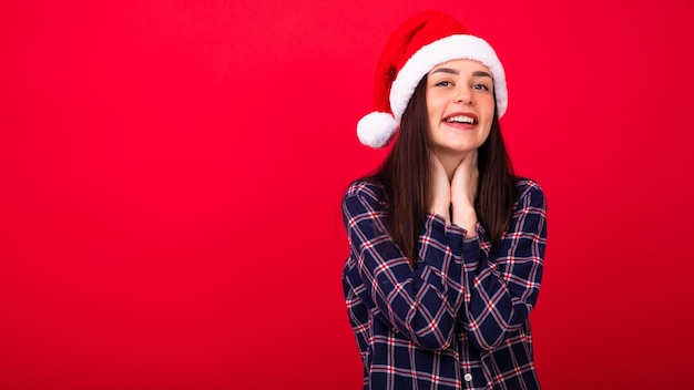 Une jeune femme en pyjama portant un chapeau de Père Noël sur fond rouge Soirée de Noël avec la famille Copy Space