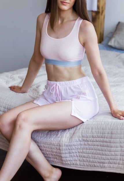Jeune femme en pyjama rose - short et haut posant sur le lit. photo