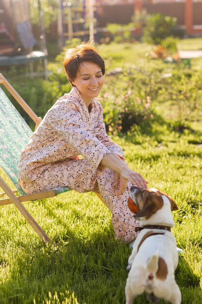 Jeune femme en pyjama se repose sur une chaise sur une pelouse verte le jour d'été ensoleillé village et vie à la campagne