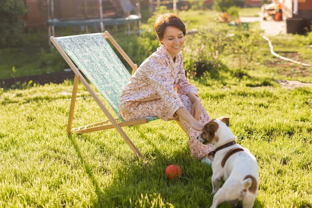 Jeune femme en pyjama se repose sur une chaise sur une pelouse verte le jour d'été ensoleillé village et vie à la campagne