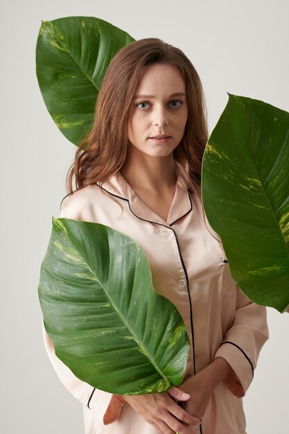 Jeune femme en pyjama de soie debout parmi de grandes feuilles vertes