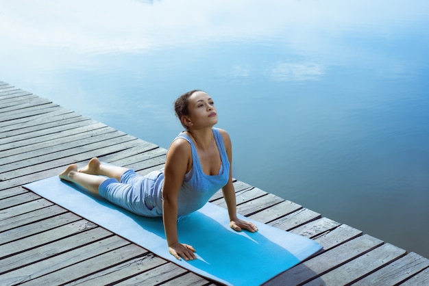 La jeune femme sur le quai faisant des asanas sur le tapis de yoga