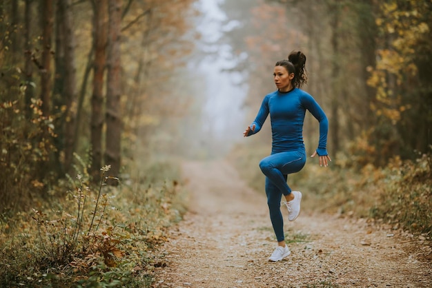 Photo jeune femme qui court faisant de l'exercice sur le sentier forestier à l'automne