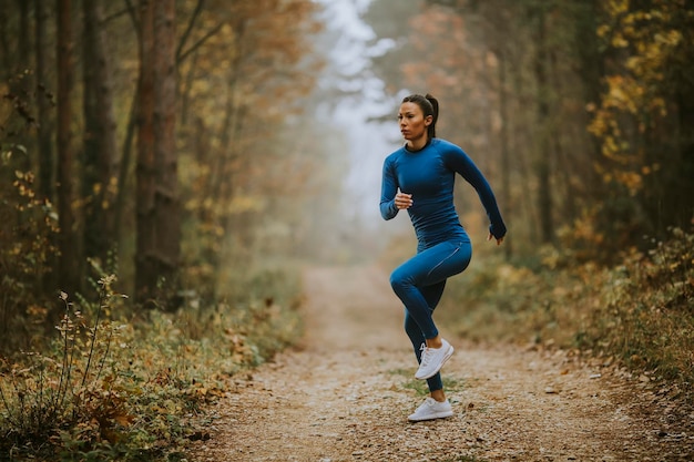 Jeune femme qui court faisant de l'exercice sur le sentier forestier à l'automne