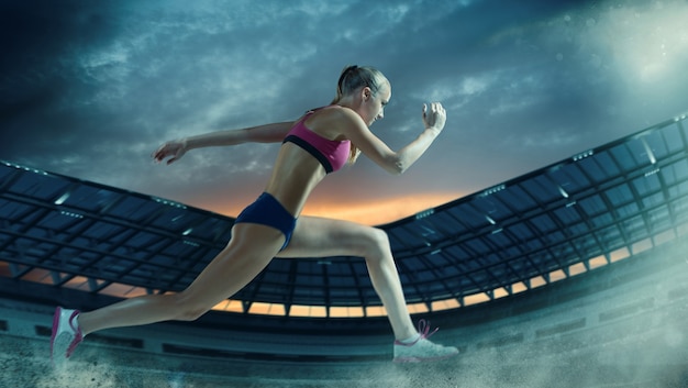 Photo jeune femme qui court sur l'hippodrome. stade d'athlétisme illuminé de nuit.