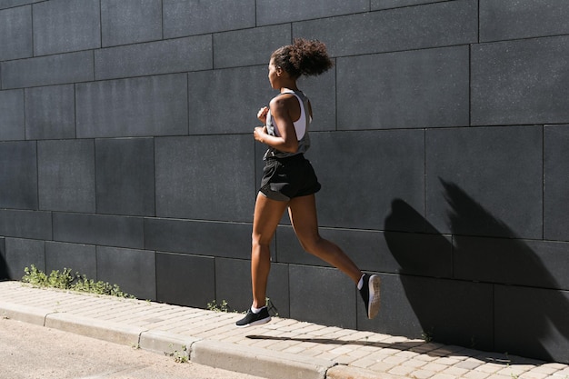 Une jeune femme qui court sur le trottoir près du mur.