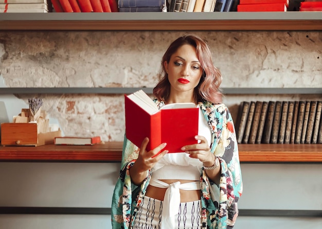 Une jeune femme qui lit un livre contre une étagère.