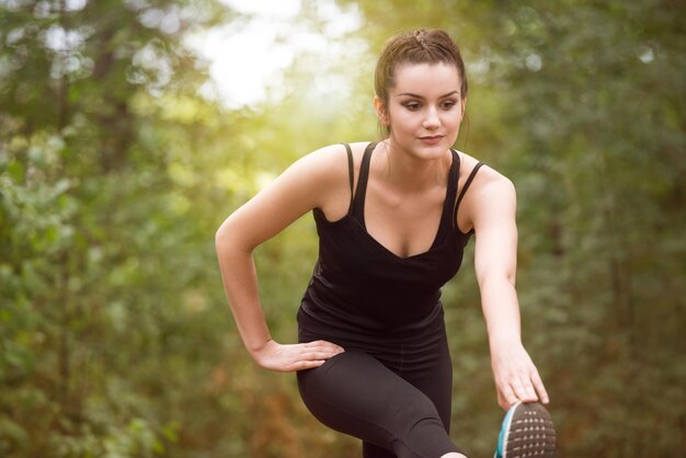 Jeune femme qui s'étend avant de courir dans la forêt boisée de formation et d'exercice pour Trail Run Marathon Endurance Fitness Mode de vie sain Concept