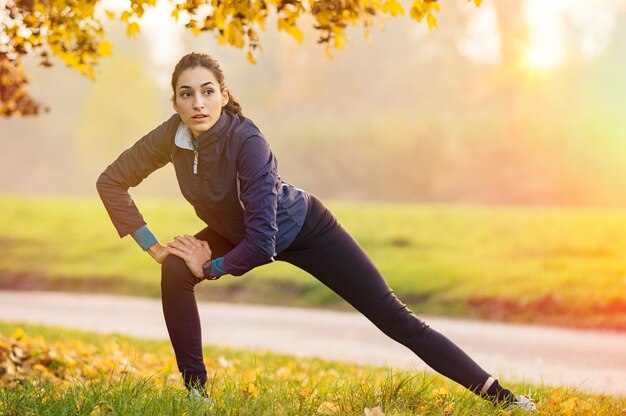 Jeune femme qui s'étend et se réchauffe au parc pendant le coucher du soleil