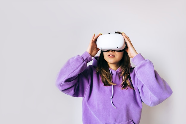 Jeune femme de race blanche à l'aide de casque VR, toucher des lunettes et levant en réalité virtuelle sur fond blanc.