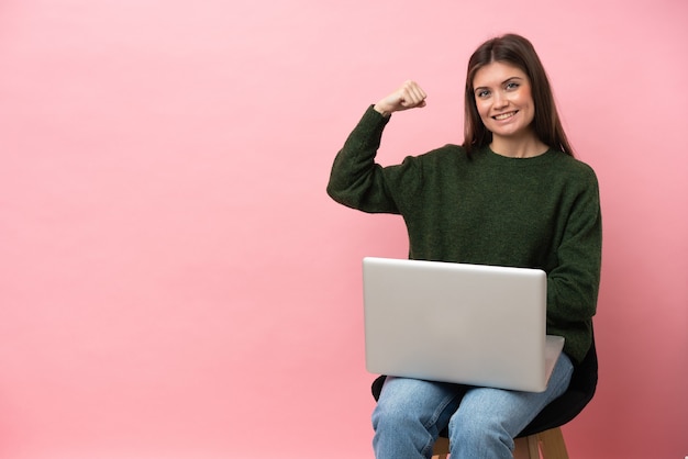 Jeune femme de race blanche assise sur une chaise avec son ordinateur portable isolé sur fond rose faisant un geste fort