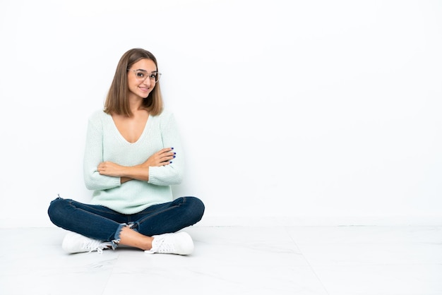 Jeune femme de race blanche assise sur le sol isolé sur fond blanc avec les bras croisés et impatient