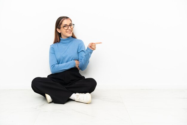 Jeune femme de race blanche assise sur le sol, pointant le doigt sur le côté