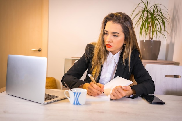 Jeune femme de race blanche blonde avec un café travaillant avec l'ordinateur