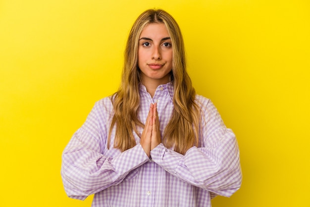 Photo jeune femme de race blanche blonde isolée sur mur jaune priant, montrant la dévotion, personne religieuse à la recherche d'inspiration divine.