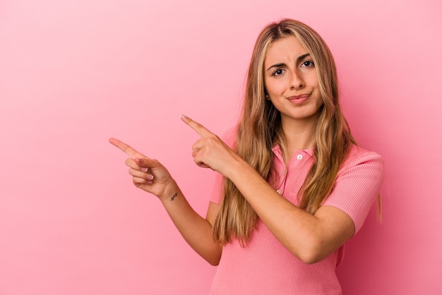 Jeune femme de race blanche blonde isolée sur un mur rose choqué de pointer avec l'index vers un espace de copie