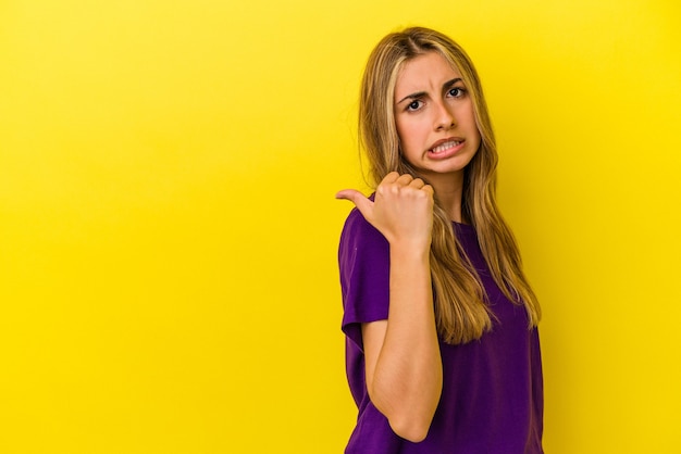 Jeune femme de race blanche blonde isolée sur les points de mur jaune avec le pouce, riant et insouciant