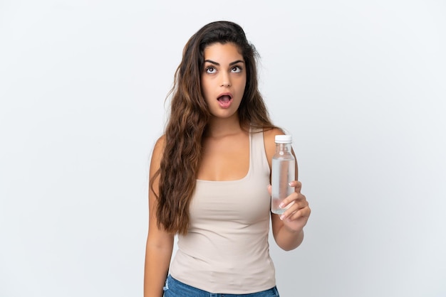 Jeune femme de race blanche avec une bouteille d'eau isolée sur fond blanc en levant et avec une expression surprise