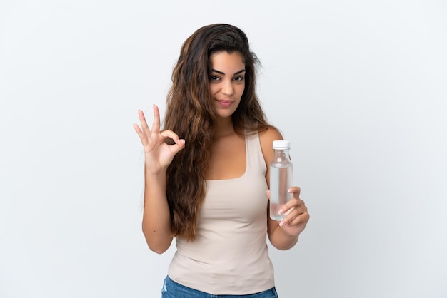 Jeune femme de race blanche avec une bouteille d'eau isolée sur fond blanc montrant un signe ok avec les doigts