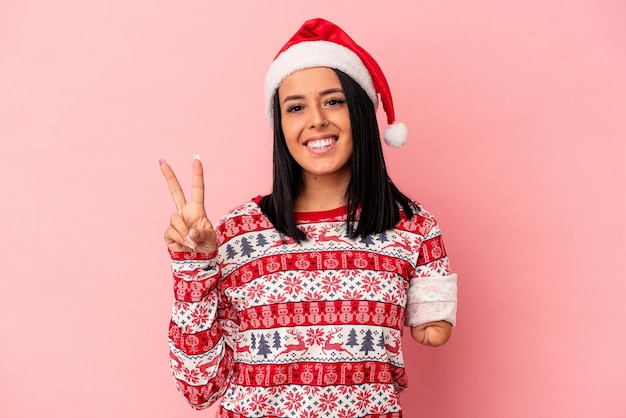 Jeune femme de race blanche avec un bras célébrant Noël isolé sur fond rose montrant le numéro deux avec les doigts.