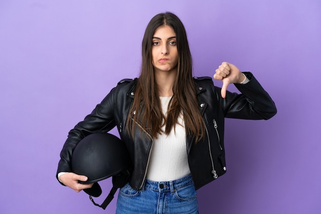 Jeune femme de race blanche avec un casque de moto isolé sur fond violet montrant le pouce vers le bas avec une expression négative