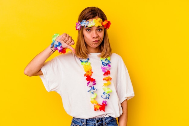 Jeune femme de race blanche célébrant une fête hawaïenne isolée sur un mur jaune montrant un geste d'aversion, les pouces vers le bas. Concept de désaccord.