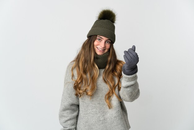 Jeune femme de race blanche avec un chapeau d'hiver isolé sur un mur blanc faisant un geste d'argent