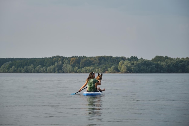 Une jeune femme de race blanche avec des dreadlocks est assise sur une planche gonflable dans le lac et pagaie avec Shepherd