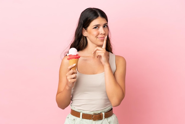 Jeune femme de race blanche avec une glace au cornet isolée sur fond rose ayant des doutes en levant les yeux