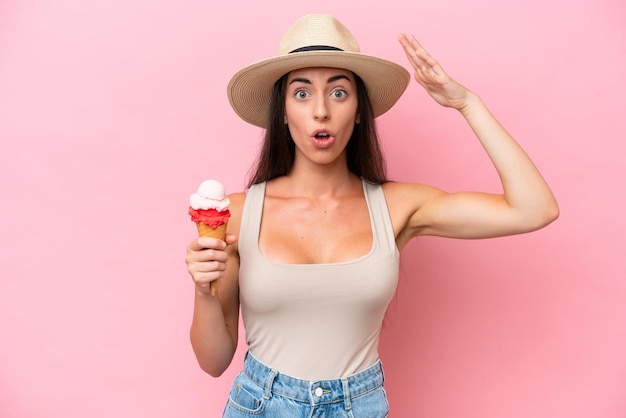 Jeune femme de race blanche avec une glace au cornet isolée sur fond rose avec une expression surprise