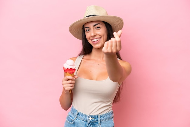 Jeune femme de race blanche avec une glace au cornet isolée sur fond rose faisant un geste d'argent