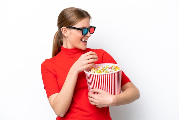 Jeune femme de race blanche isolée sur fond blanc avec des lunettes 3D et tenant un grand seau de pop-corn tout en regardant côté