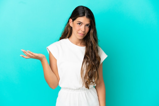 Jeune femme de race blanche isolée sur fond bleu faisant des doutes geste