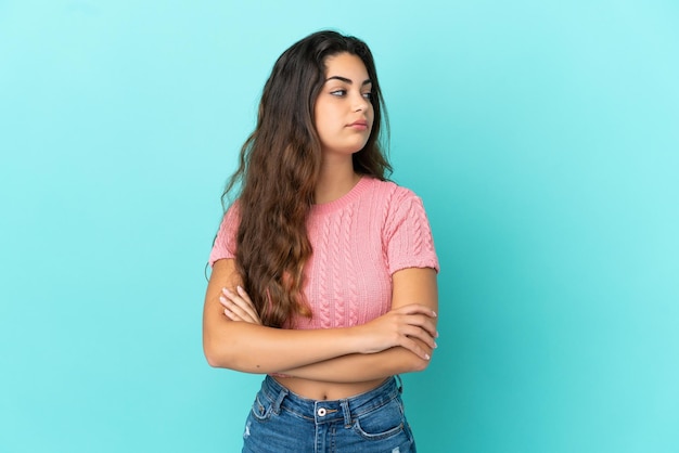 Jeune femme de race blanche isolée sur fond bleu en gardant les bras croisés