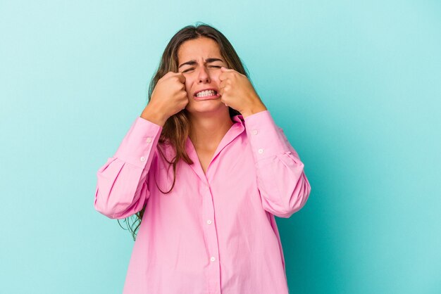 Jeune femme de race blanche isolée sur fond bleu pleurnichant et pleurant de manière inconsolable.