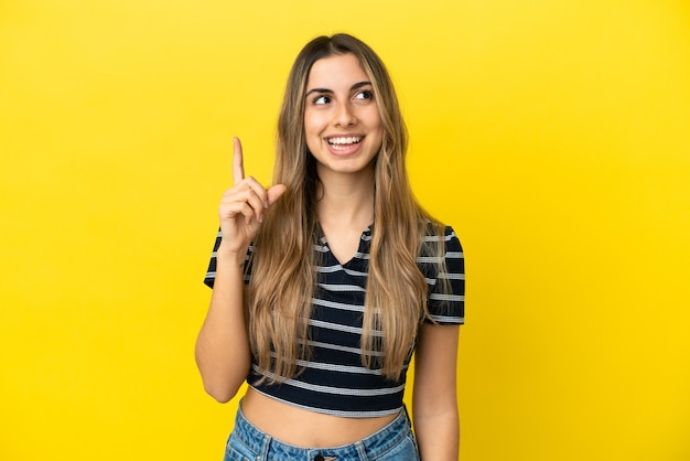 Jeune femme de race blanche isolée sur fond jaune dans l'intention de réaliser la solution tout en soulevant un doigt