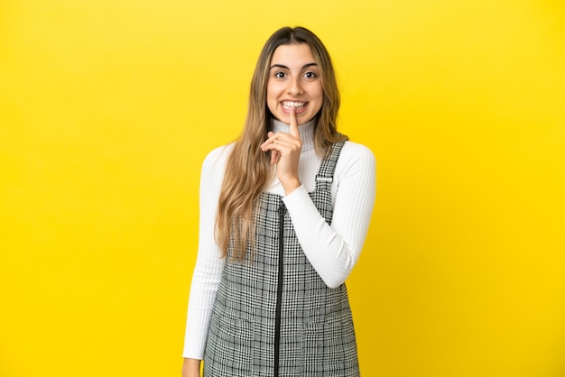 Jeune femme de race blanche isolée sur fond jaune montrant un signe de silence geste mettant le doigt dans la bouche