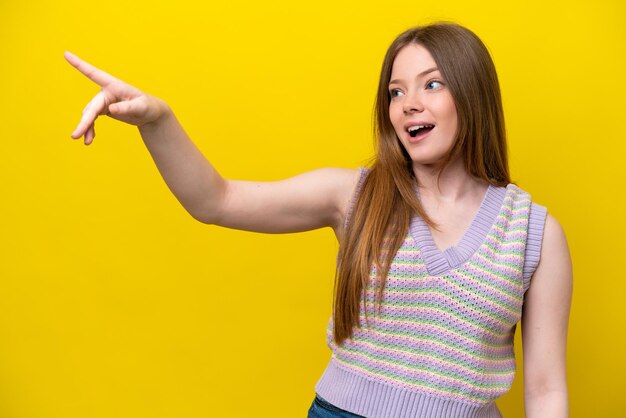 Jeune femme de race blanche isolée sur fond jaune pointant vers l'extérieur