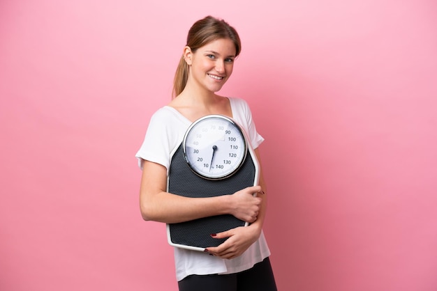 Jeune femme de race blanche isolée sur fond rose avec une machine de pesage