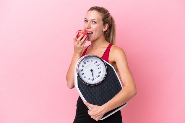 Jeune femme de race blanche isolée sur fond rose avec une machine à peser et avec une pomme