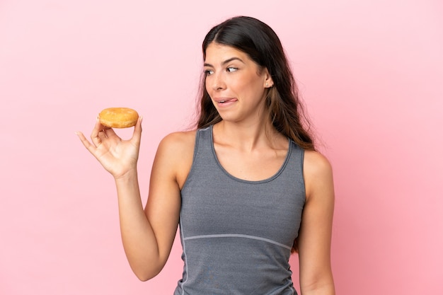 Jeune femme de race blanche isolée sur fond rose tenant un beignet