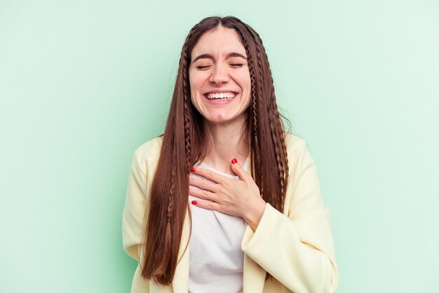 Jeune femme de race blanche isolée sur fond vert éclate de rire en gardant la main sur la poitrine.