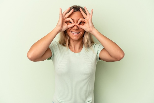 Photo jeune femme de race blanche isolée sur fond vert montrant un signe d'accord sur les yeux