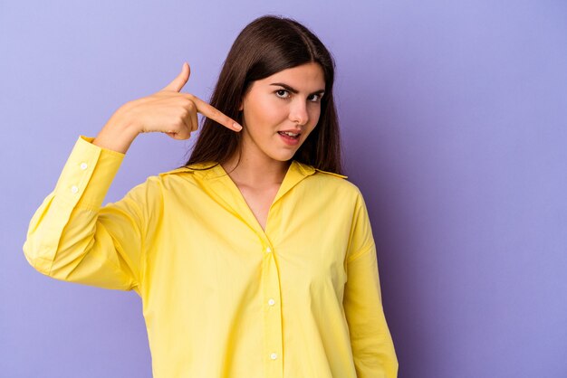 Jeune femme de race blanche isolée sur fond violet personne pointant à la main vers un espace de copie de chemise, fier et confiant