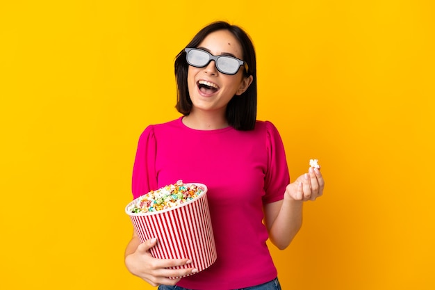 Jeune femme de race blanche isolée avec des lunettes 3D et tenant un grand seau de pop-corn