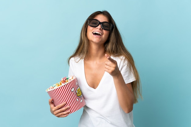 Jeune femme de race blanche isolée avec des lunettes 3D et tenant un grand seau de pop-corn