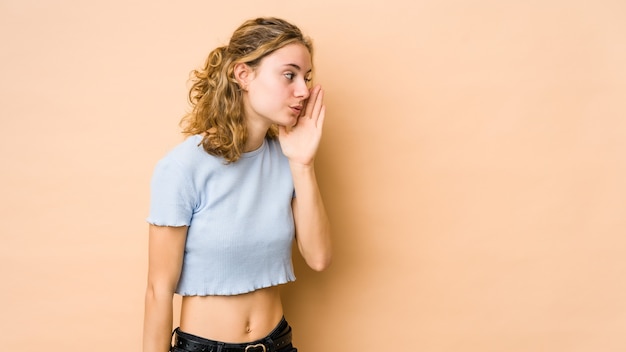 Jeune femme de race blanche isolée sur un mur beige dit une nouvelle secrète de freinage à chaud et à côté