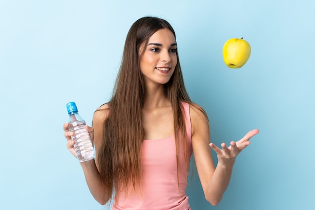 Jeune femme de race blanche isolée sur un mur bleu avec une pomme et une bouteille d'eau